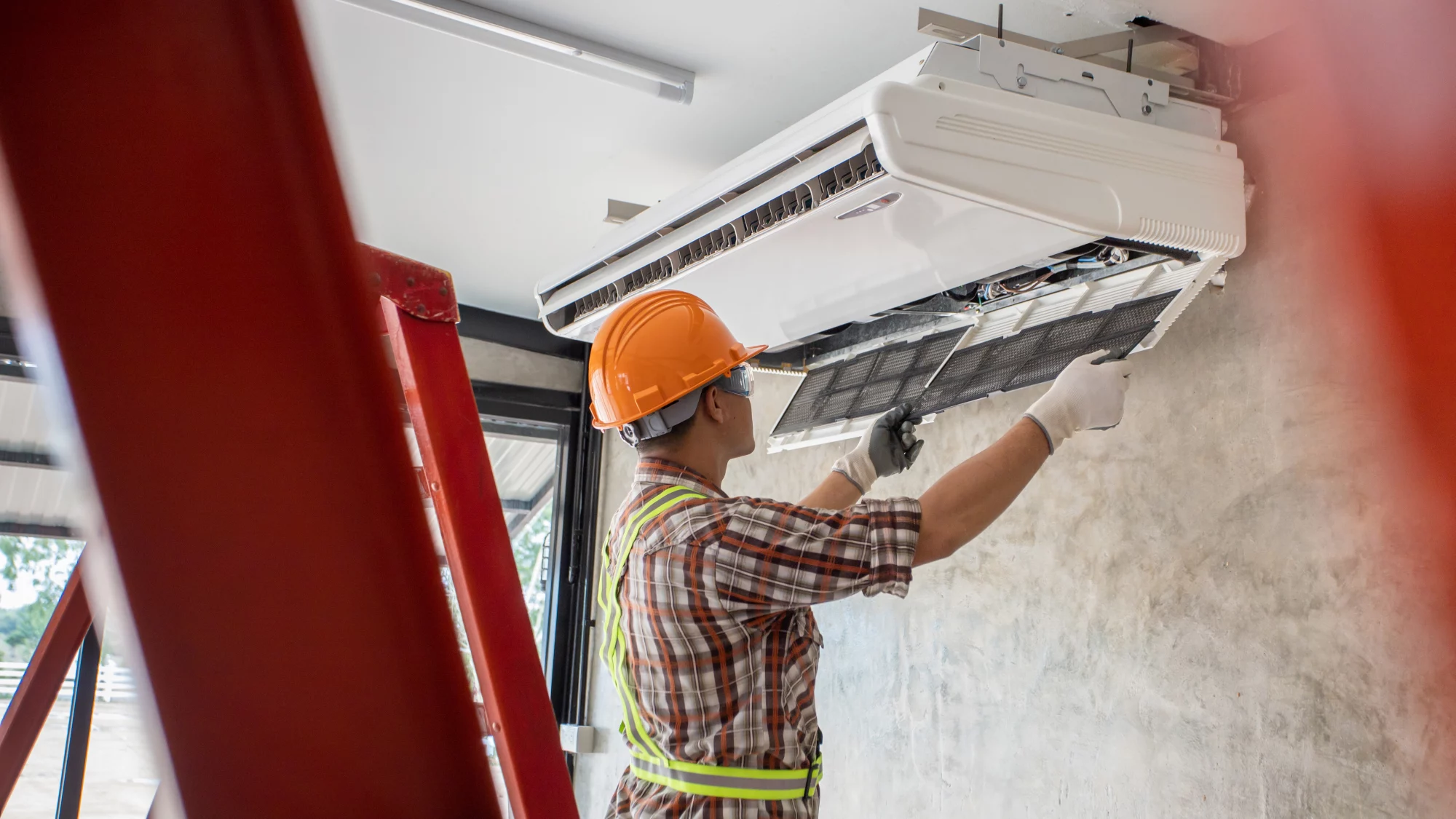image with a men mounting a new split system of water cooled air conditioning ceiling mounted unit and checking the filters before first start. Man is with a construct ppe hat and installation is in a new constructed commercial building.