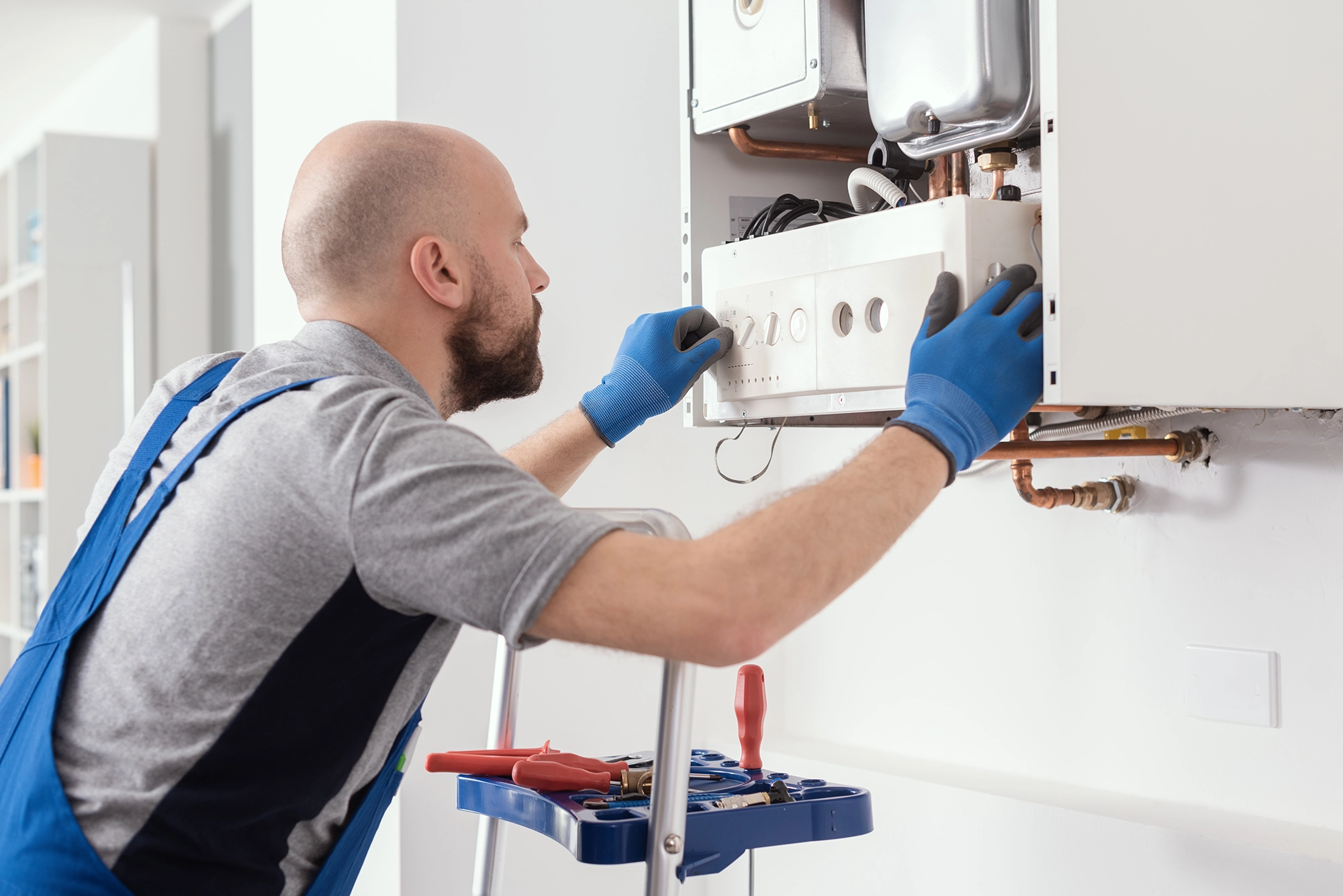 Image of an engineer with a beard and blue gloves inspecting a boiler in a white room, after completing a powerflush service.