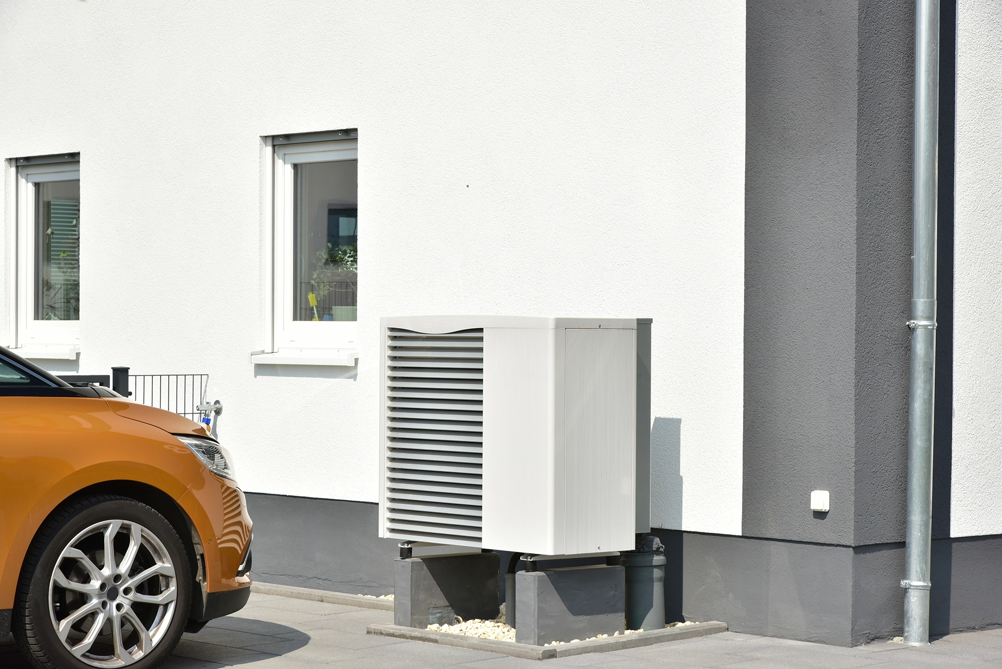 Image of an outdoor air source heat pump unit next to a parked car, being inspected after a powerflushing procedure.